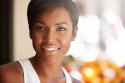 Portrait of beautiful happy young black model with short pixie hairstyle and healthy clean skin looking and smiling at the camera with cheerful expression, showing her white teeth, posing outdoors