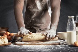 Image of hard working male cook or baker with dark skin wears apron, sheets well made dough, going to bake tart, isolated over black chalk background. Unrecognizable African American chef on kitchen