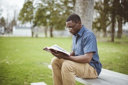 A young African-American male sitting on the bench and reading the Bible