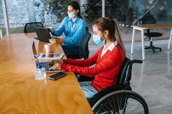 Young latin woman in wheelchair working with another woman colleague at workplace or office in Mexico city