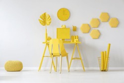 Pouf next to chair at desk with monstera leaf against white wall with honeycombs in yellow room interior