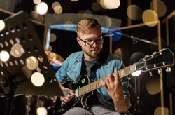 music, people, musical instruments and entertainment concept - male guitarist playing electric guitar at studio rehearsal over festive lights