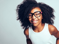Happy little African girl with long curly hair wearing glasses while standing by herself against a gray background