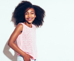 Cheerful young African girl with long curly hair smiling confidently while standing alone against a white background