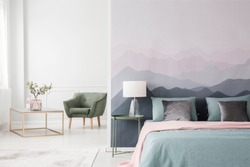 Large bed with blue sheets and a pink blanket by a landscape wallpaper in a cozy, modern bedroom interior