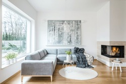 White sitting room interior with grey corner sofa, tulips in vase placed on an end table, fireplace and modern art painting