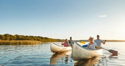Two smiling young couples paddling canoes together on a still lake on a sunny summer afternoon