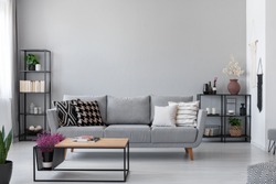 Copy space on the wall of scandinavian living room with modern couch, metal shelves and industrial coffee table, real photo