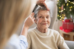 A health visitor combing hair of senior woman at home at Christmas time.