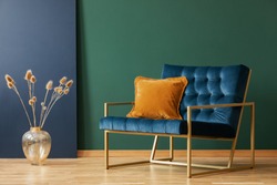 Brown cushion on blue armchair in green living room interior with flowers in gold vase. Real photo