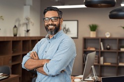 Portrait of happy mature businessman wearing spectacles and looking at camera. Multiethnic satisfied man  feeling confident in a creative office. Successful middle eastern business man smiling.