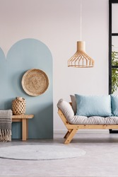 Wicker chandelier above wooden Scandinavian sofa with futon in bright living room interior