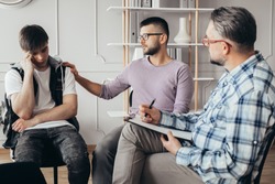 Young man in glasses comforting his depressed friend during meeting with counselor