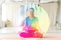 mindfulness, spirituality and healthy lifestyle concept - woman meditating in lotus pose at yoga studio over rainbow aura
