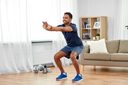 sport and healthy lifestyle concept - smiling indian man with fitness tracker exercising and doing squats at home