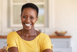 Mature happy woman smiling and looking at camera. Portrait of african american woman in casual clothing and curly short hair relaxing at home.  Portrait of successful black lady with copy space.