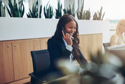 Laughing young African American businesswoman talking on a telephone while working at an office reception desk with a colleague 
