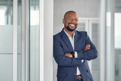 Mature cheerful african american executive businessman at workspace. Portrait of smiling ceo at modern office workplace in suit looking at camera. Happy leader standing in front of company building.