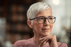 Beautiful senior business woman thinking and wearing spectacles. Thoughtful old woman teacher looking away with eyeglasses. Closeup face of mature pensive lady contemplating the future with copy space