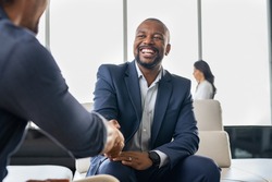 Two happy mature business men shaking hands in office. Successful african american businessman in formal clothing closing deal with handshake. Multiethnic businessmen shaking hands during a meeting.