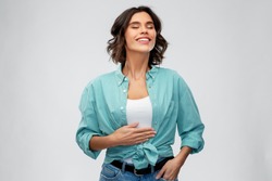 digestion, eating people concept - happy smiling full young woman in turquoise shirt touching her tummy over grey background