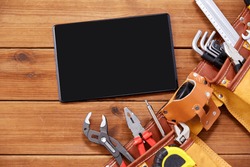 repair, building and renovation concept - tablet pc computer and belt with different work tools in pockets on wooden boards background