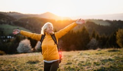 Front view of senior woman hiker standing outdoors in nature at sunset.