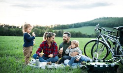 Family with two small children on cycling trip, sitting on grass and resting.