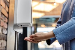 hygiene, health care and safety concept - close up of woman using hand sanitizer from dispenser at shopping mall