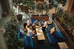 High angle of a diverse group of young businesspeople talking together during a casual meeting the the lounge area of an office