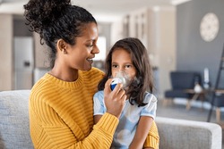 Little indian girl making inhalation with nebulizer with lovely mother. Woman makes inhalation to a sick child while embracing her. Mom helping daughter with cold and flu to inahale nebuliser aerosol.