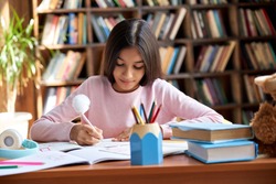 Cute smart hispanic indian preteen kid girl student, latin child primary school pupil studying at table, doing homework at home, writing task, taking notes, learning sitting at classroom desk.