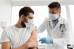 medicine, vaccination and healthcare concept - doctor wearing face protective medical mask for protection from virus disease with syringe doing injection of vaccine to male patient