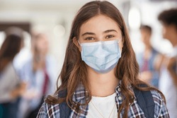 Portrait of girl wearing a face mask standing in college campus and looking at camera. University young woman smiling despite the Covid-19 pandemic. Satisfied and proud student girl with surgical mask