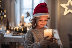 Happy small girl standing indoors at Christmas, holding candle.
