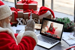 Over shoulder view of Santa Claus video calling kid girl on laptop greeting child by webcam talk open Christmas gift box in virtual online chat meeting using computer sit at workshop table on xmas.
