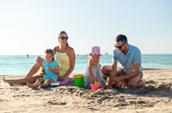 family and leisure concept - happy father, mother and daughters on summer beach