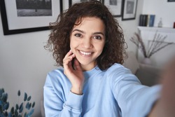 Happy pretty hispanic gen z teen girl holding smartphone looking at camera taking selfie shot for social media, making video call at home by virtual mobile app. Close up face headshot portrait.