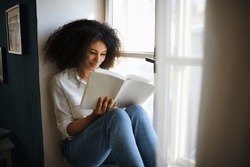 Portrait of young woman with book indoors at home, reading.