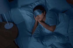 people, relax and comfort concept - young african american woman in eye mask sleeping in bed at home at night