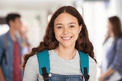 Portrait of beautiful college student standing in hallway school while looking at camera. Intelligent university girl with backpack smiling. Proud and satisfied teen in high school corridor standing.