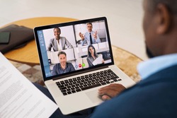 Black businessman talking to his team about plan in video conference from home. Group of business people using laptop for an online meeting in video call during covid lockdown.