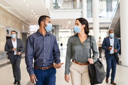 Indian business man and businesswoman walking with face mask and talking at modern workspace. Two colleagues wearing protective mask due to covid-19 while going to work, new normal concept. 