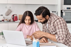 Indian dad helping school child teen daughter studying online at home. Father and kid girl elearning having virtual class on laptop, studying remote homeschool on computer, doing homework together.