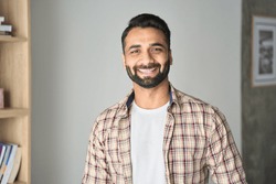 Headshot portrait of attractive confident indian Hispanic man with toothy smile looking at camera at modern living room. Latin businessman posing in casual stylish look at home office.