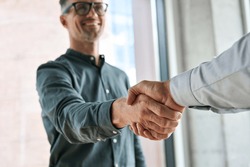 Two happy diverse professional business men executive leaders shaking hands at office meeting. Smiling businessman standing greeting partner with handshake. Leadership, trust, partnership concept.