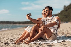 technology, leisure and people concept - happy couple taking selfie by smartphone on summer beach