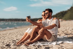 technology, leisure and people concept - happy couple taking selfie by smartphone on summer beach