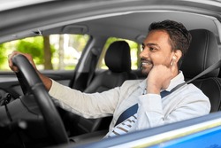 transport, people and technology concept - smiling indian man or driver with wireless earphones or hands free device driving car