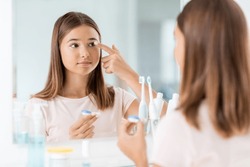 health, vision and old people concept - teenage girl applying contact lenses in front of mirror at home bathroom